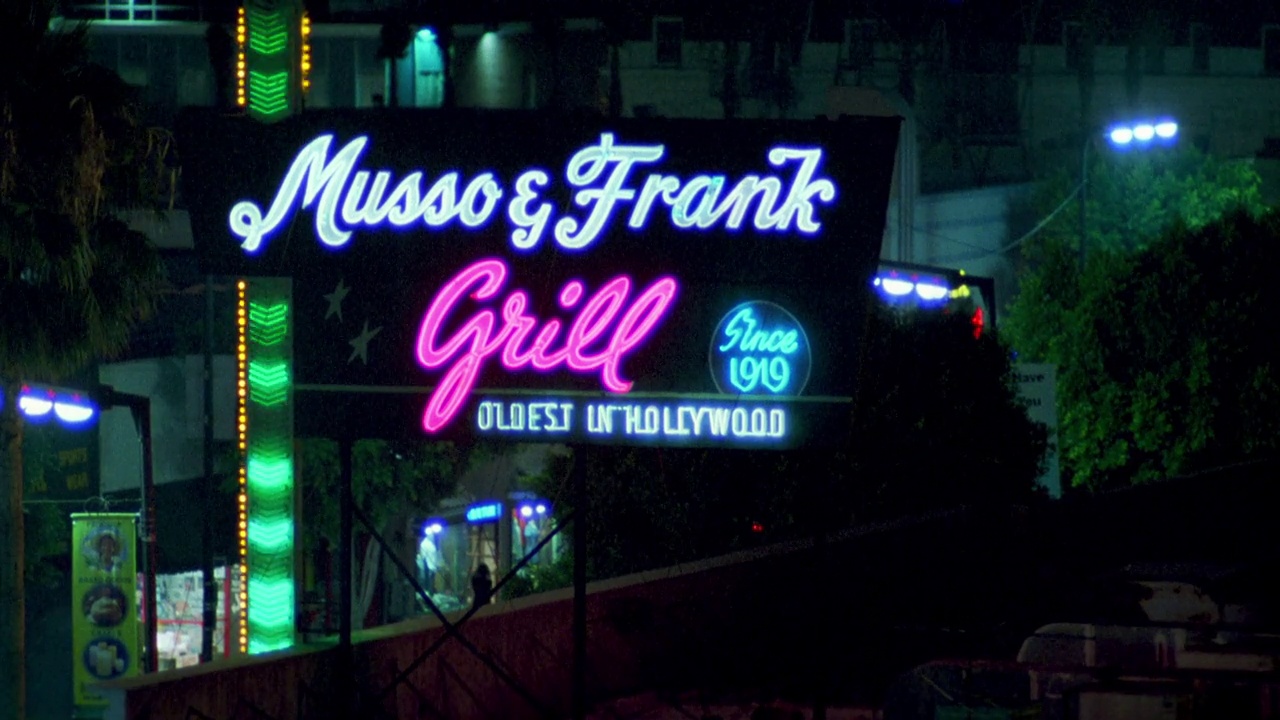 从“musso & frank grill”的广告牌从右到左，到霓虹灯招牌“musso & frank grill”。好莱坞的大街。bg的灯光和商店。有通风口的屋顶。城市区域。视频素材