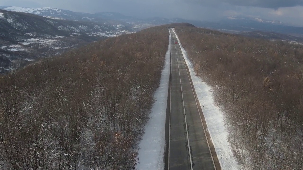 在塞尔维亚Knjazevac附近的冬季，在白雪皑皑的山脉上行驶的公路上的汽车的高角度鸟瞰无人机视频视频素材