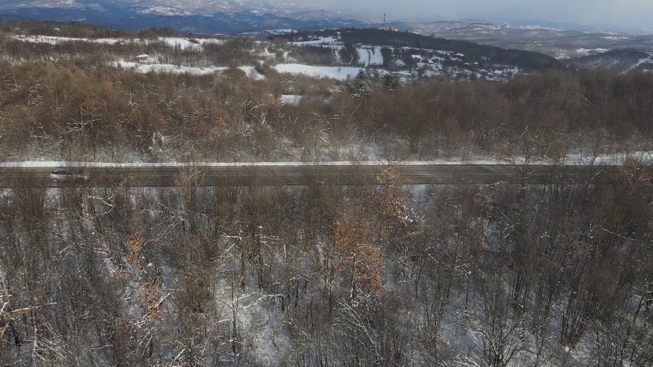 在塞尔维亚Knjazevac附近的冬季，在白雪皑皑的山脉上行驶的公路上的汽车的高角度鸟瞰无人机视频视频素材