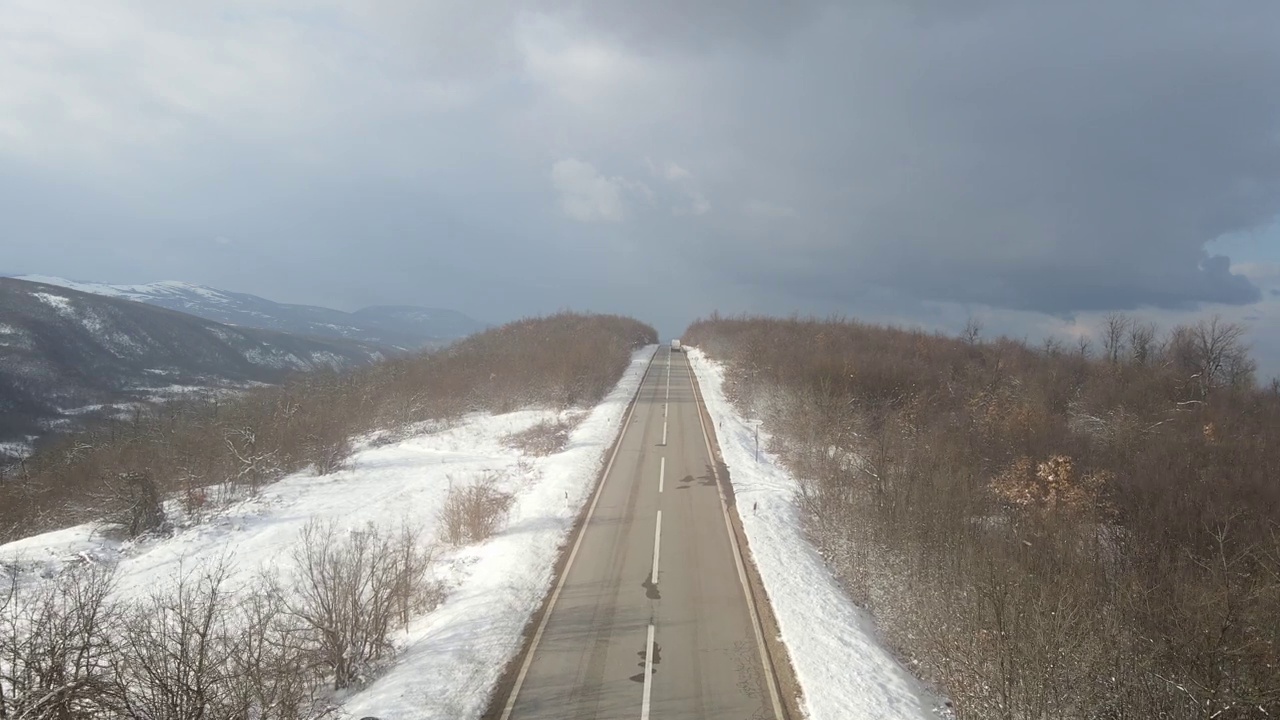 在塞尔维亚Knjazevac附近的冬季，在白雪皑皑的山脉上行驶的公路上的汽车的高角度鸟瞰无人机视频视频素材