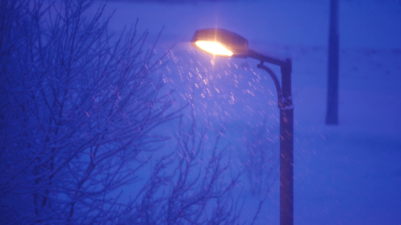 在冬天的夜晚，路灯照亮飘落的雪花。视频素材