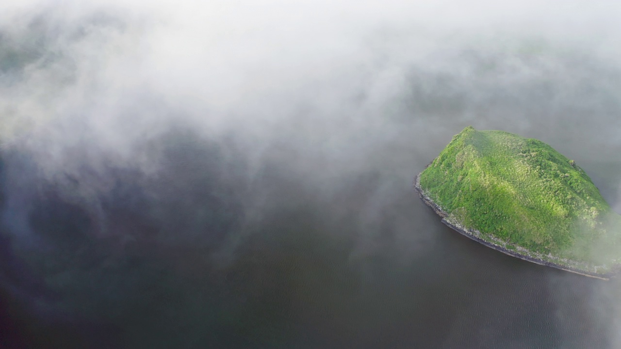 空中全景。碧绿的小岛掩藏在浓雾的云里，在黑暗的水面上飞翔视频下载