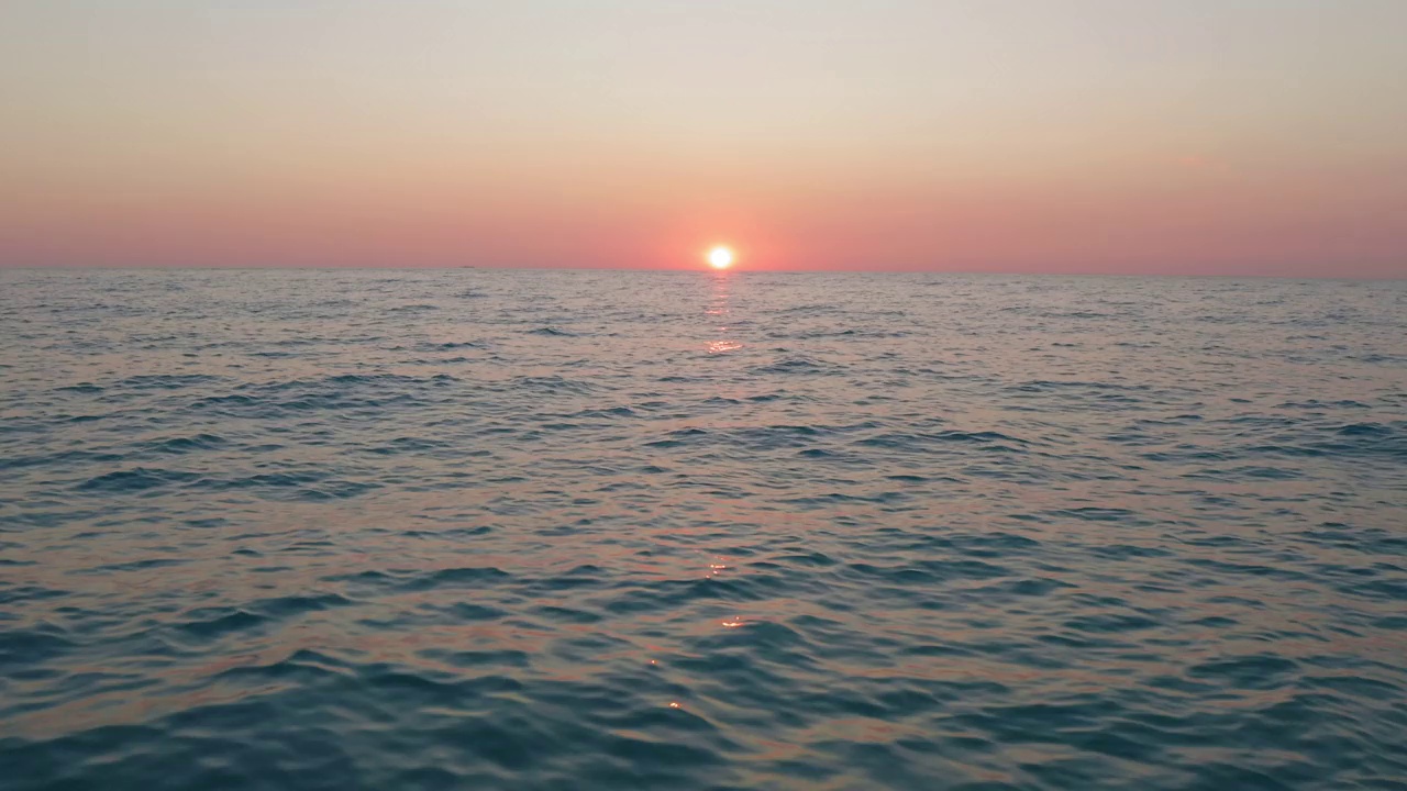 夕阳西下，天空泛着橘黄色，海浪平静的海面上的空中飞行。视频素材