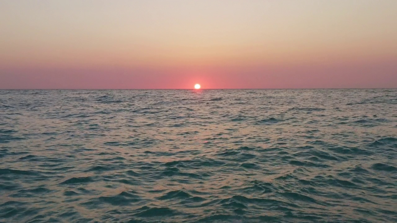 夕阳西下，天空泛着橘黄色，海浪平静的海面上的空中飞行。视频素材