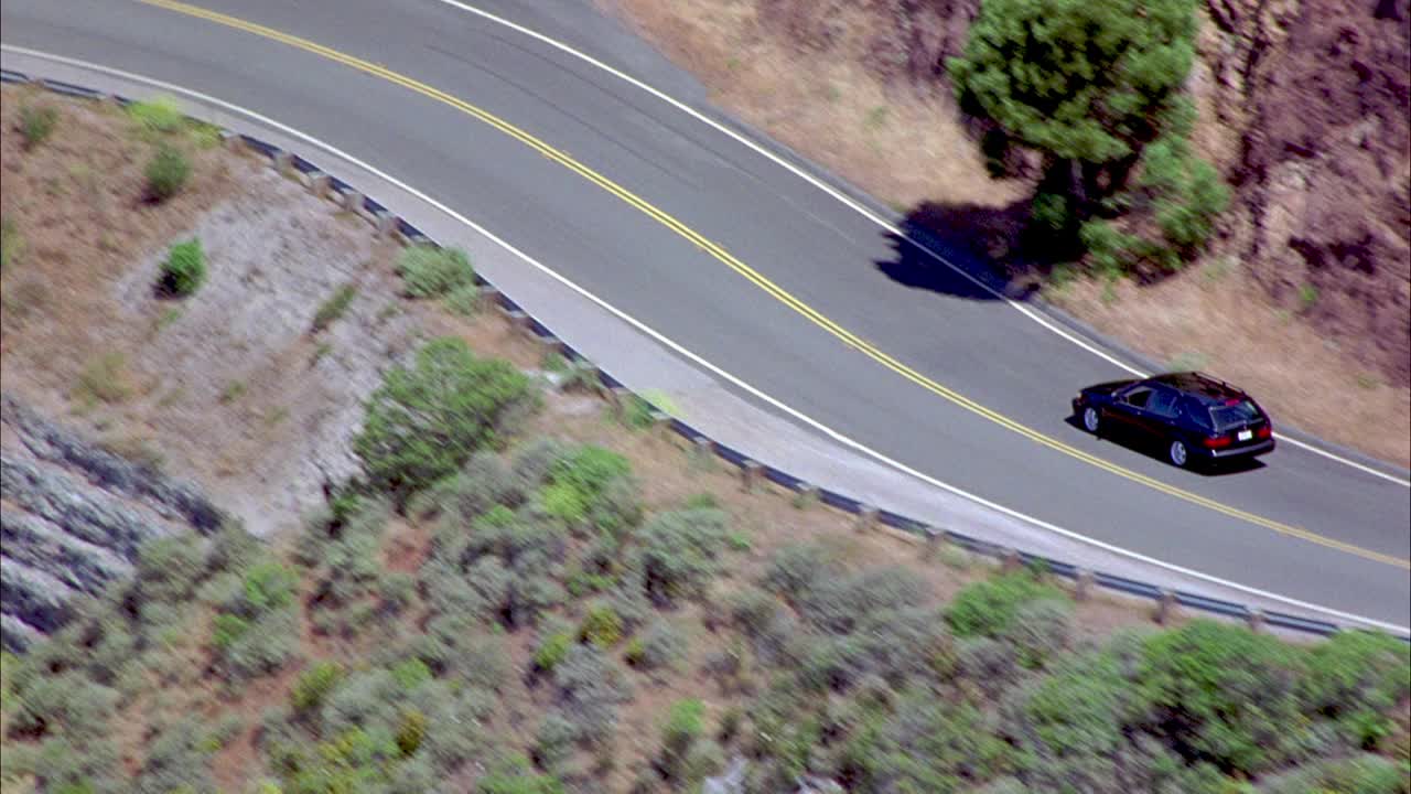 空中跟随黑色旅行车在山区弯道上行驶。看看山上生长的植被。视频素材