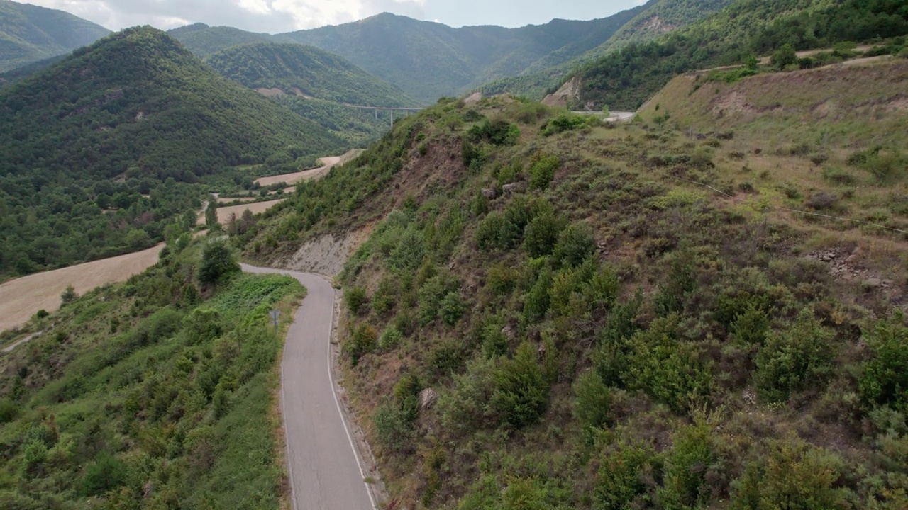 美丽的无人机视图沥青道路在高山上。山脉消失在天空中，天空略有多云，但山峰被太阳照亮。视频素材