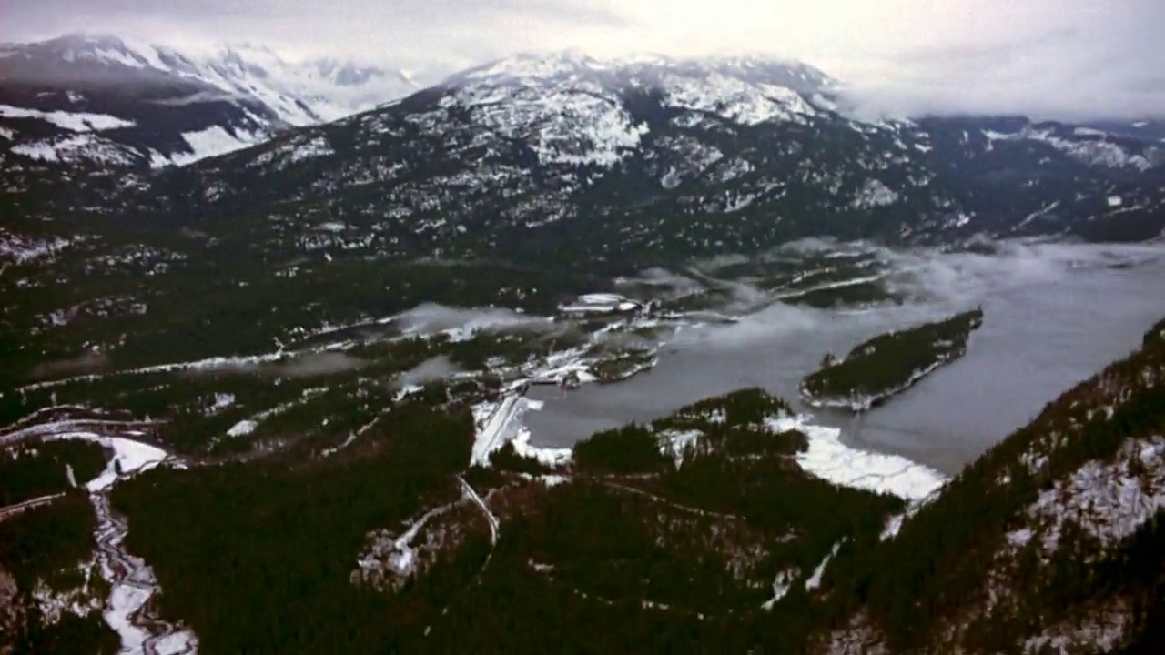 在雪山上空飞行。看那绿油油的松树，上面撒满了雪。天空是厚厚的白色的雾和云。视角以令人眼花缭乱的方式前后倾斜。看到下面覆盖着白雪的圆形山丘和山脉。视频素材