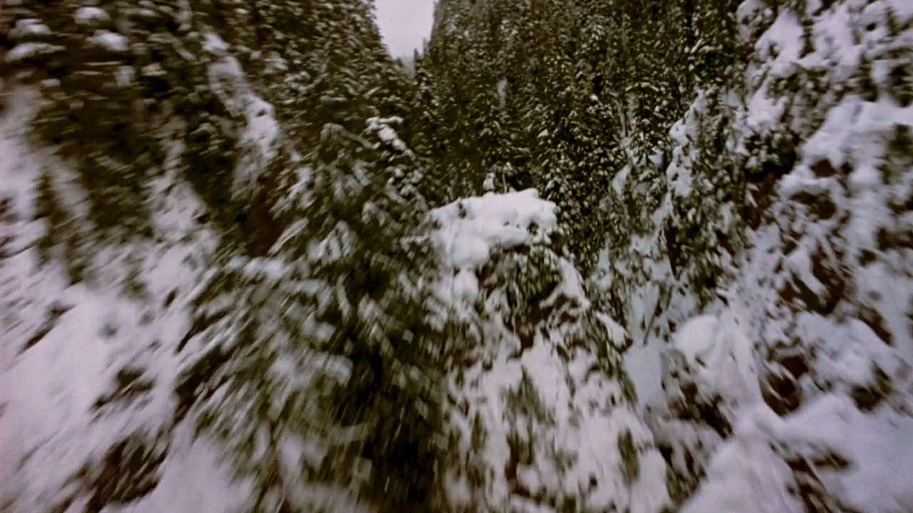 空中穿越雪山。镜头从喷气式飞机快速穿越山脉的角度旋转而来。看那绿油油的松树，上面撒满了雪。天空是厚厚的白色的雾和云。飞机飞过山谷。视频素材