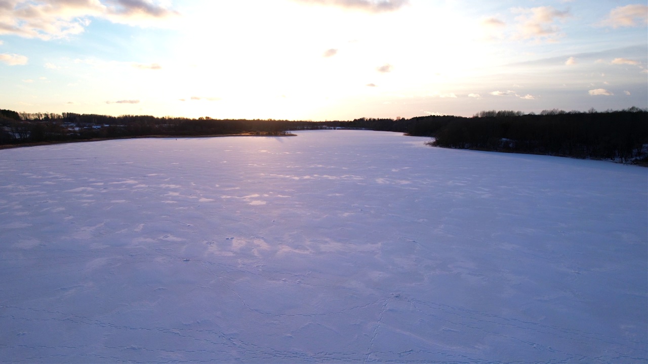 在冬季鸟瞰森林中冰冻的湖泊。冰天雪地的湖面在阳光的映衬下。视频素材