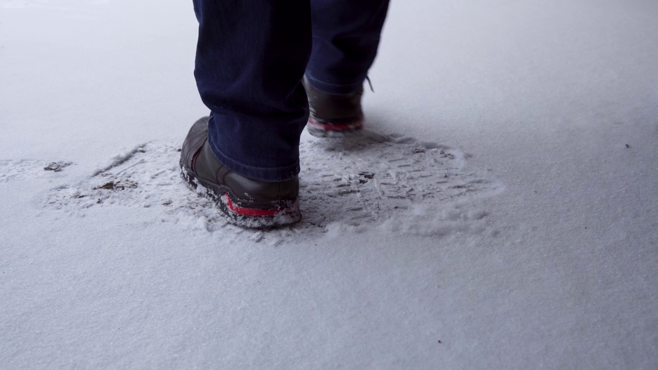 雪地上穿着黑色靴子的男人的腿。他跳舞取暖，然后走出镜头，留下脚印。视频素材