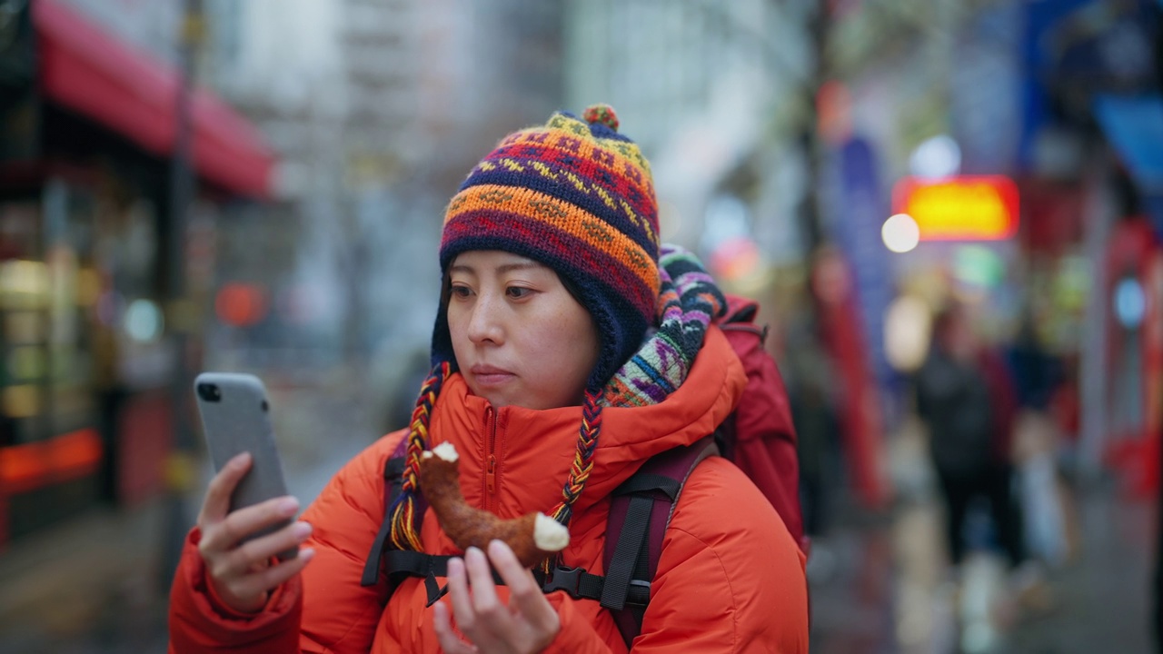 年轻的女性游客在冬天的城市里享受当地的食物，用智能手机自拍视频素材