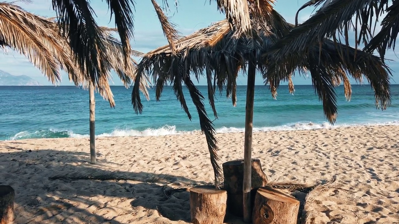 希腊的爱琴海海滩，棕榈树枝做成的伞，以水为背景。慢动作视频素材