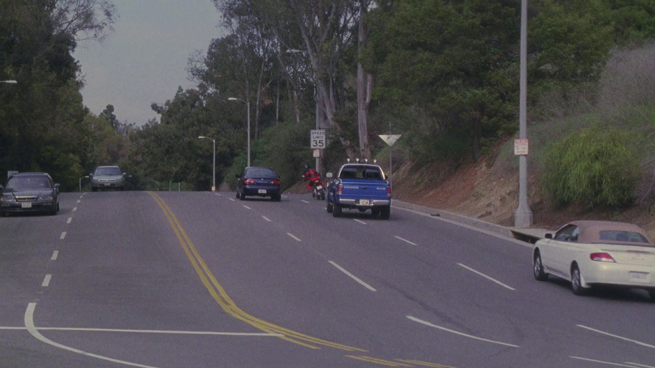 广角的蓝色道奇达科他卡车后面的摩托车下山的林荫道路或街道。卡车和摩托车在路上与其他汽车相撞。可能是飞车追逐。22 FPS。视频素材