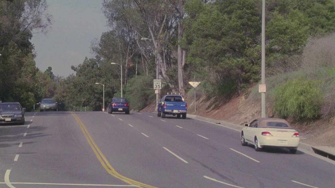 广角的蓝色道奇达科他卡车后面的摩托车下山的林荫道路或街道。卡车和摩托车在路上与其他汽车相撞。可能是飞车追逐。22 FPS。视频素材