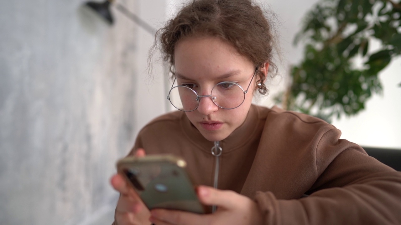 有智能手机的聪明孩子。严肃漂亮的女孩戴着眼镜玩手机视频素材