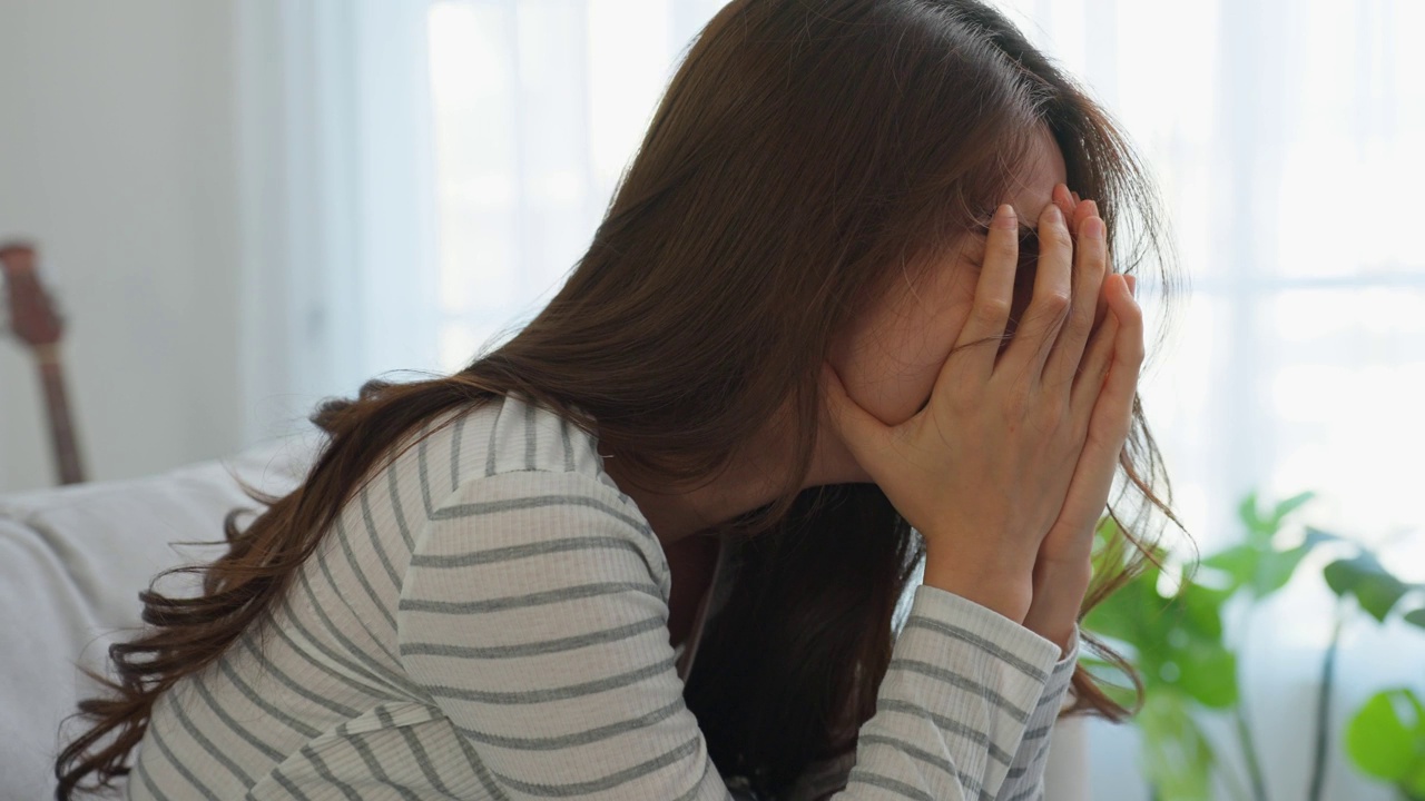 亚洲美女不开心的女人坐在沙发上感到沮丧和压力。有心理问题的有魅力的忧虑女性，在家里感到焦虑、抑郁、不安和悲伤。视频素材