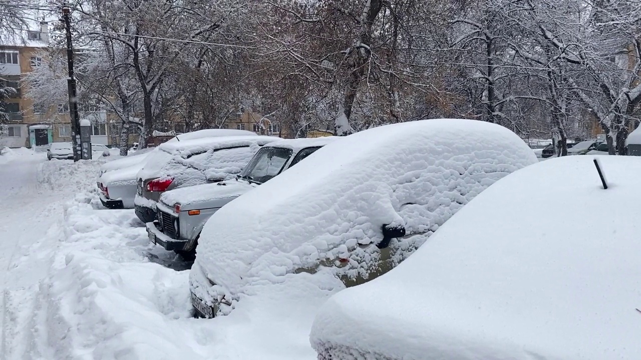 跟踪拍摄院子里被大雪覆盖的汽车。雪堆在街上和汽车上。视频素材