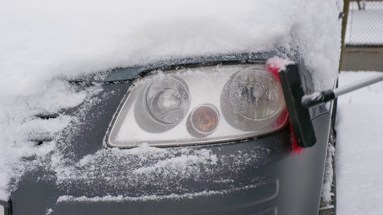 冬天，一名男子拿着刷子在车上清理积雪。早晨，汽车被雪覆盖着视频素材