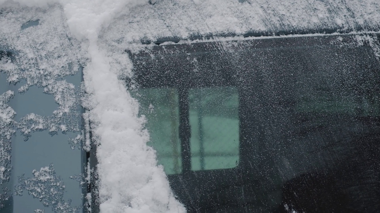 一个男人用刷子从他的车里刷雪。在寒冷的冬日里擦车窗视频素材