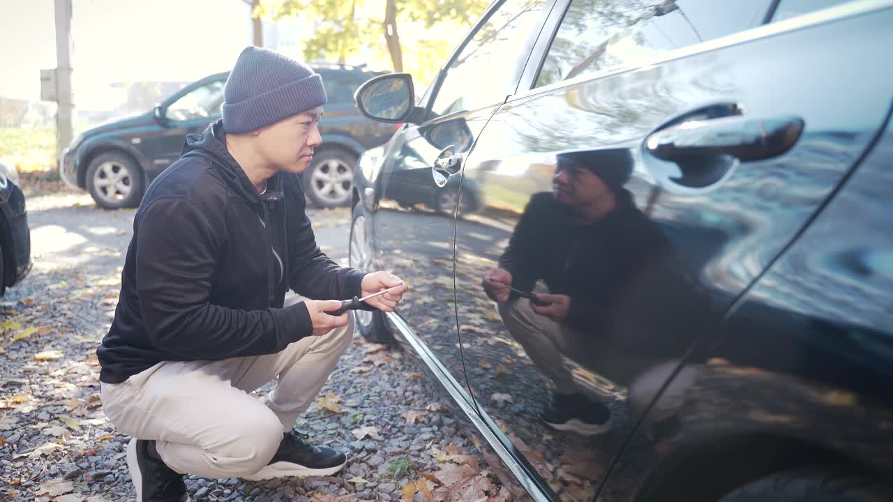 男贼抢了车，用螺丝刀打开车门，从中间走了进去。窃贼在停车场没有安保人员的情况下擅自闯入一辆汽车视频素材