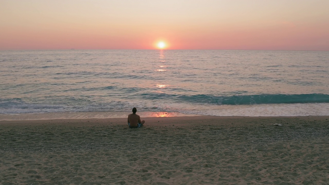 空中静态的男子剪影在海滩上。海水表面平静的波浪在日落黄昏发光的橙色天空。视频素材