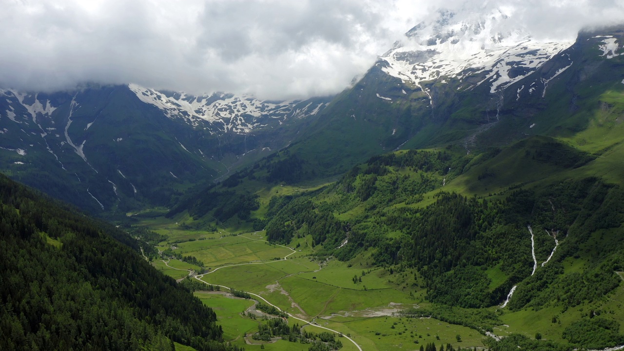 美丽的风景绿色草地在山谷包围阿尔卑斯山雪山山脉在夏天的一天风景奥地利空中慢向前运动视频购买