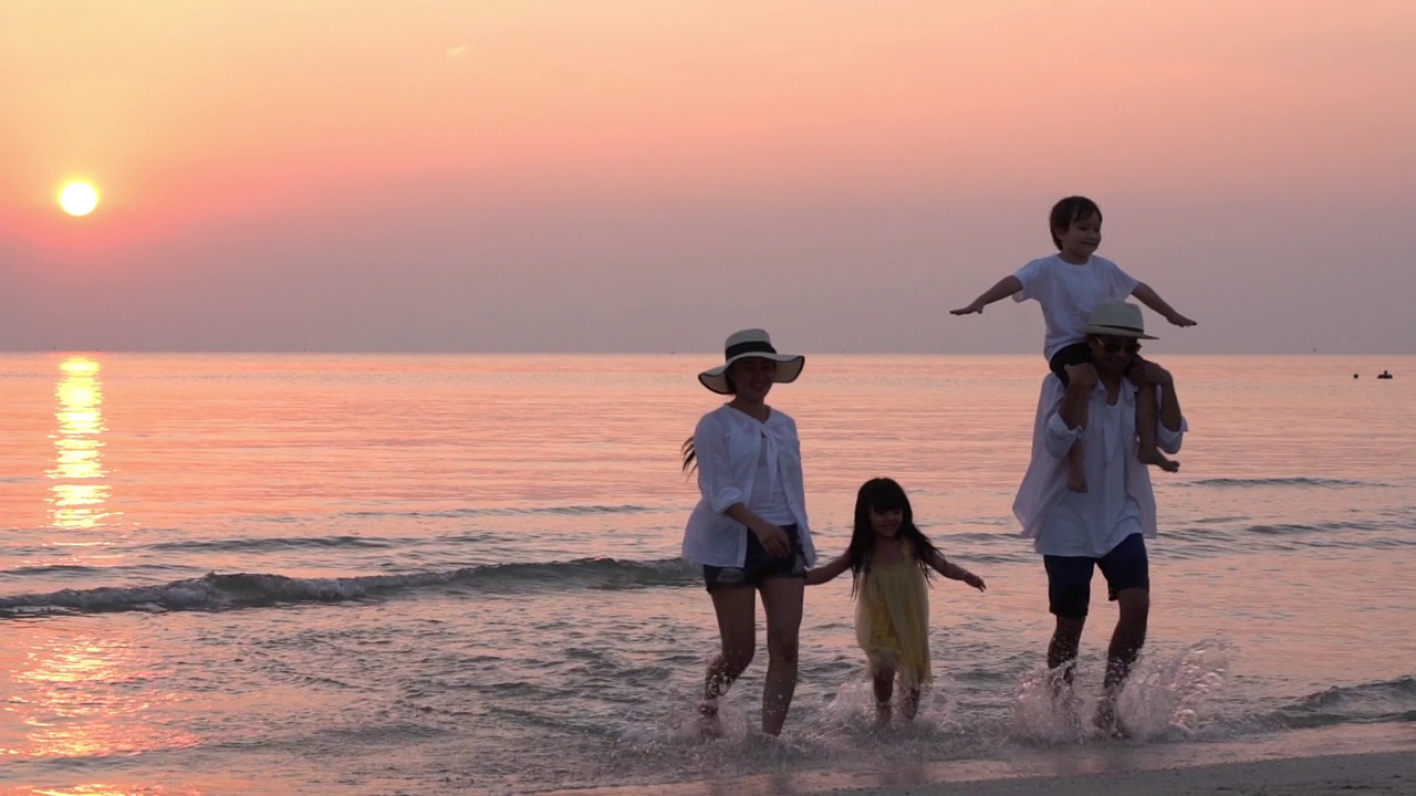 一个亚洲家庭在夕阳下的沙滩上玩耍视频素材