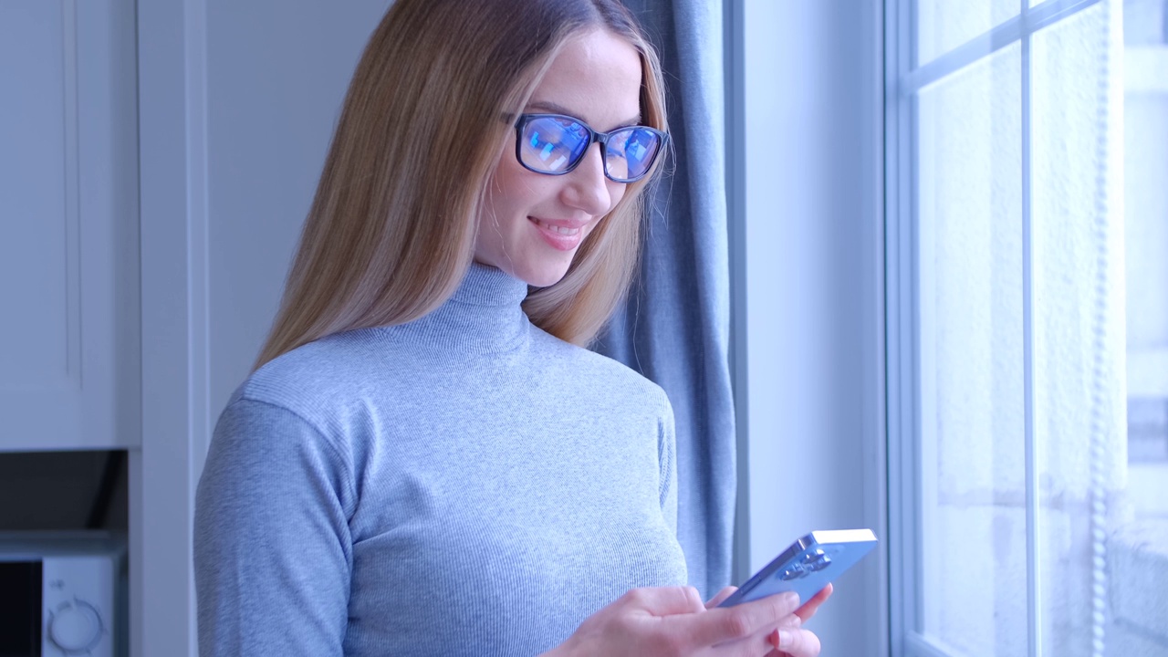 漂亮的金发女人在手机应用程序中输入信息。有吸引力的白人女性在家中使用现代智能手机进行在线交流视频素材