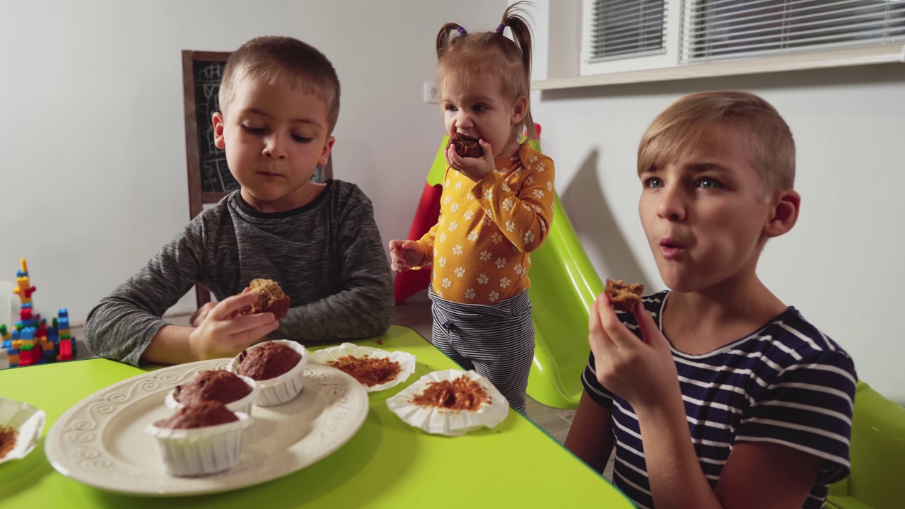 不同年龄的孩子在家吃松饼。幼儿园里的孩子吃纸杯蛋糕的时候很有食欲。视频素材