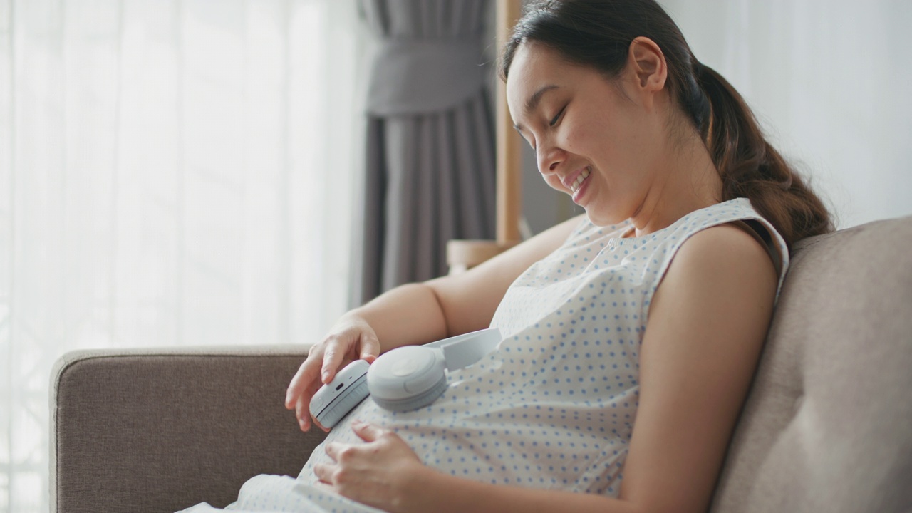 年轻女子用耳机罩住怀孕的肚子视频素材