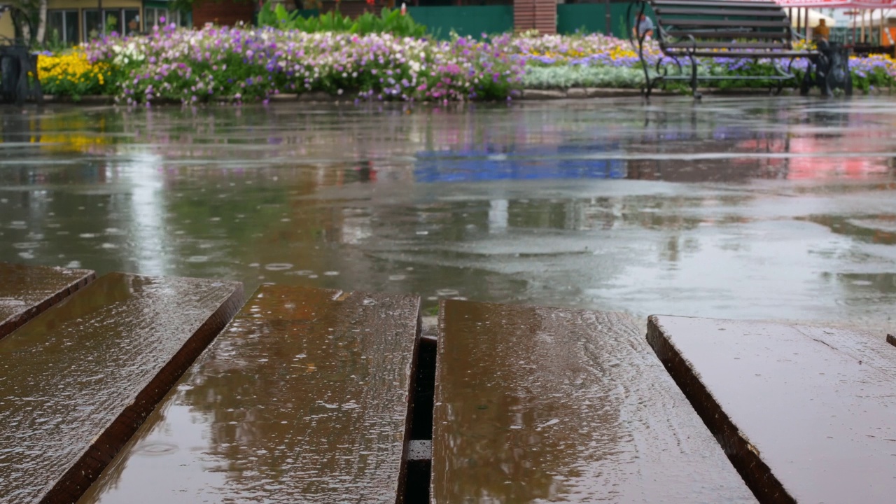 雨在城市公园里，雨点落在露台的木地板和道路的沥青上。城里天气不好，你可以在阳台上避雨。多雨的城市概念视频素材