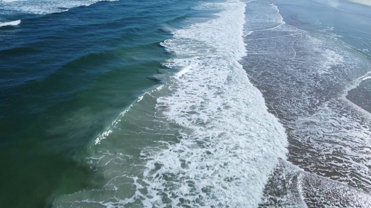 从柔和的海浪上鸟瞰，飞过沙滩上的浪花视频素材