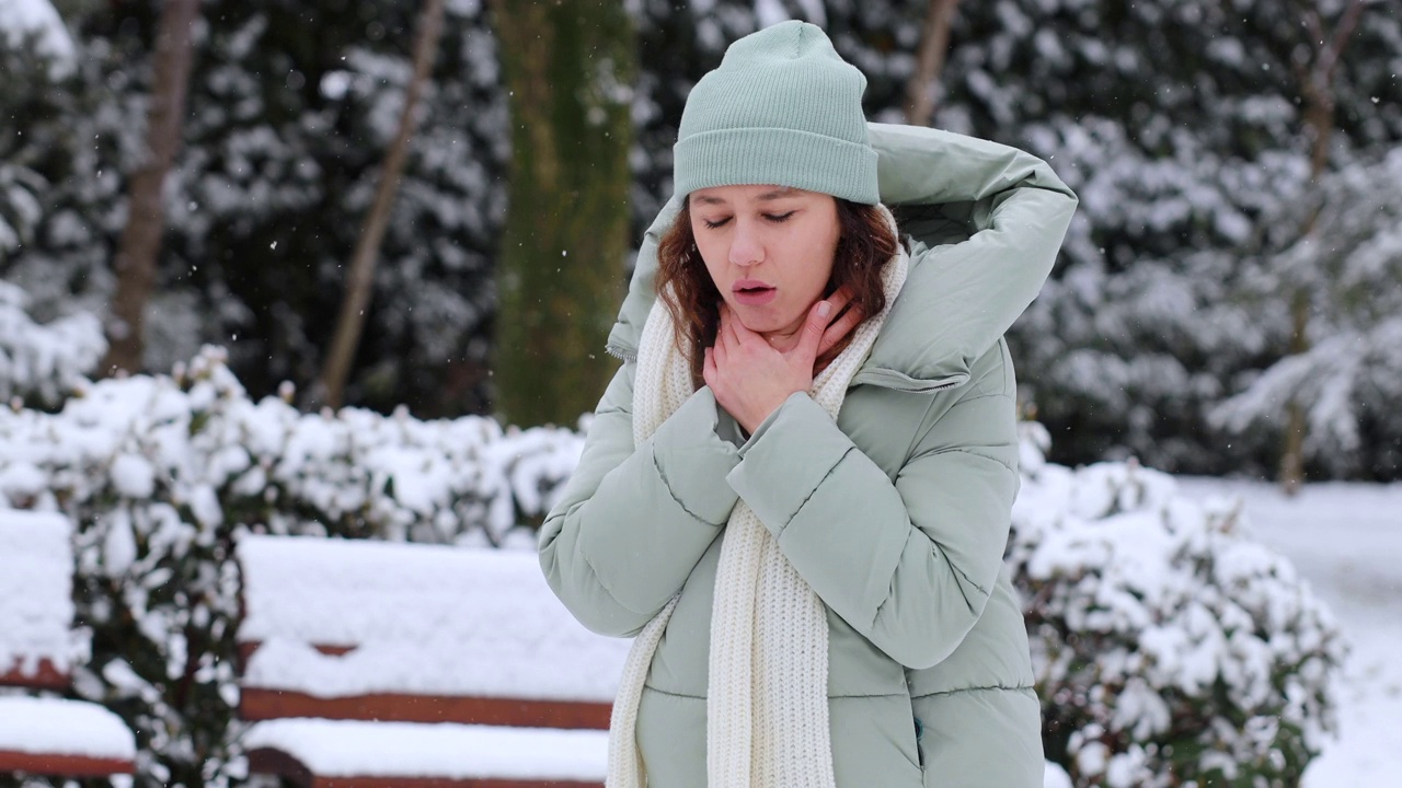 在一个寒冷的雪天，生病的年轻女子在公园里咳嗽视频素材