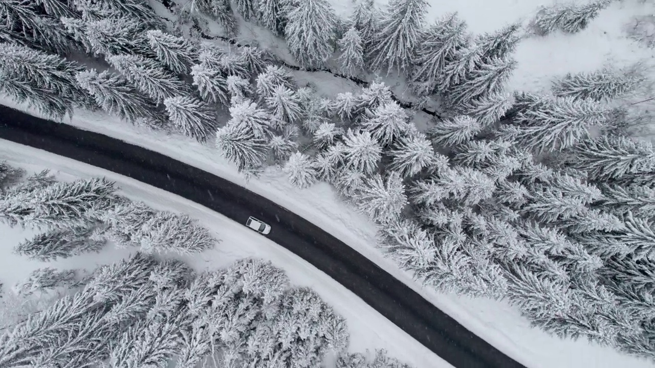 空中拍摄的白色汽车沿着道路行驶在冬天的雪原森林。冬天开车旅行，天气恶劣时开车视频素材