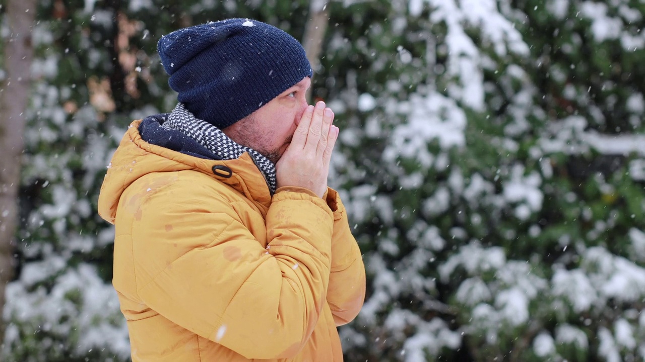 一个年轻人在雪天的街道上暖手视频素材