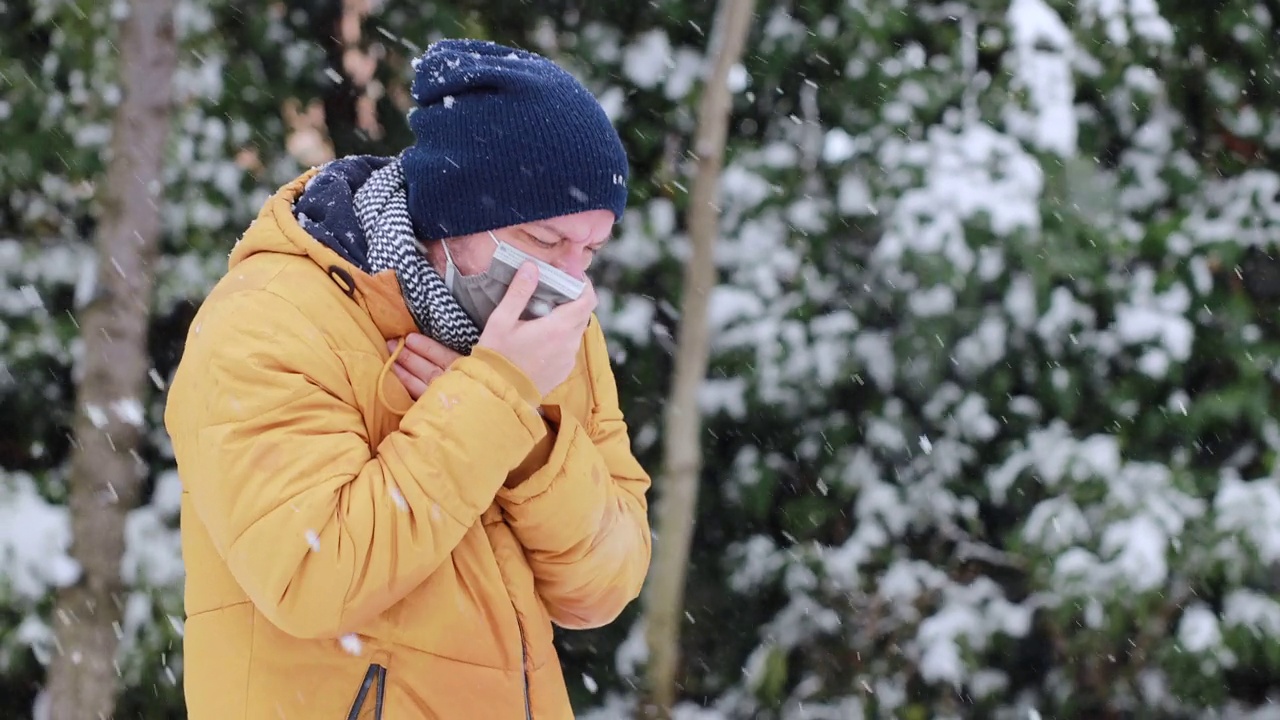 一个生病的年轻人在一个寒冷的雪天在公园里咳嗽视频素材