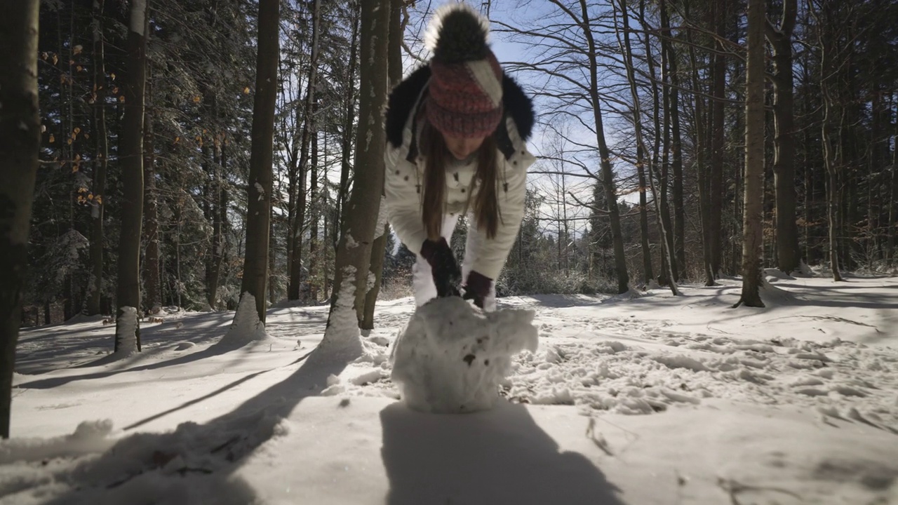 在一个阳光明媚的冬日，一个十几岁的女孩正在森林里堆雪人。视频素材