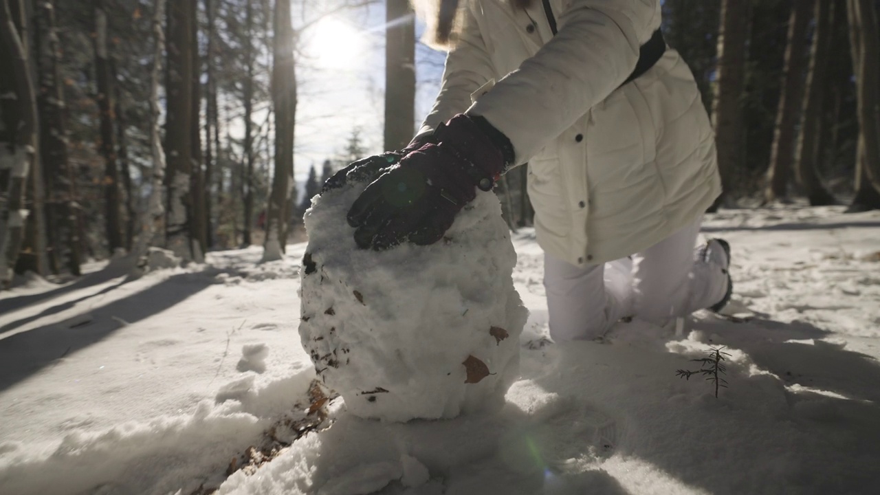 在一个阳光明媚的冬日，一个十几岁的女孩正在森林里堆雪人。视频素材