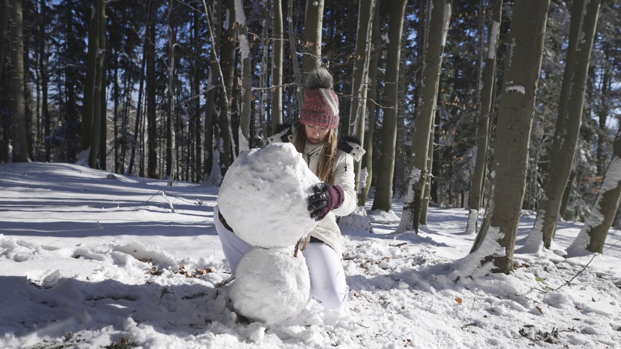 在一个阳光明媚的冬日，一个十几岁的女孩正在森林里堆雪人。视频素材