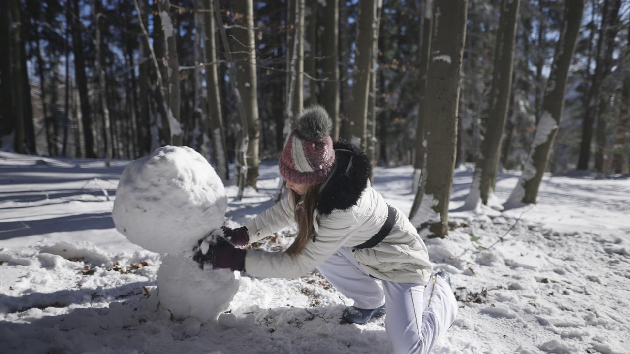 在一个阳光明媚的冬日，一个十几岁的女孩正在森林里堆雪人。视频素材