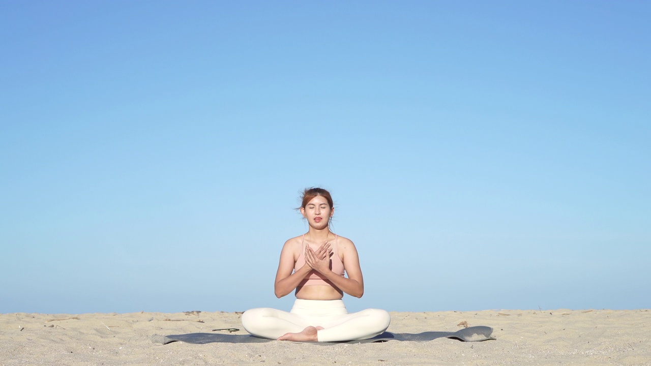 亚洲女人在海边边聊天和做瑜伽，背景是海浪的海洋，在日落时在海边冥想，使她的心平静和和平。视频素材