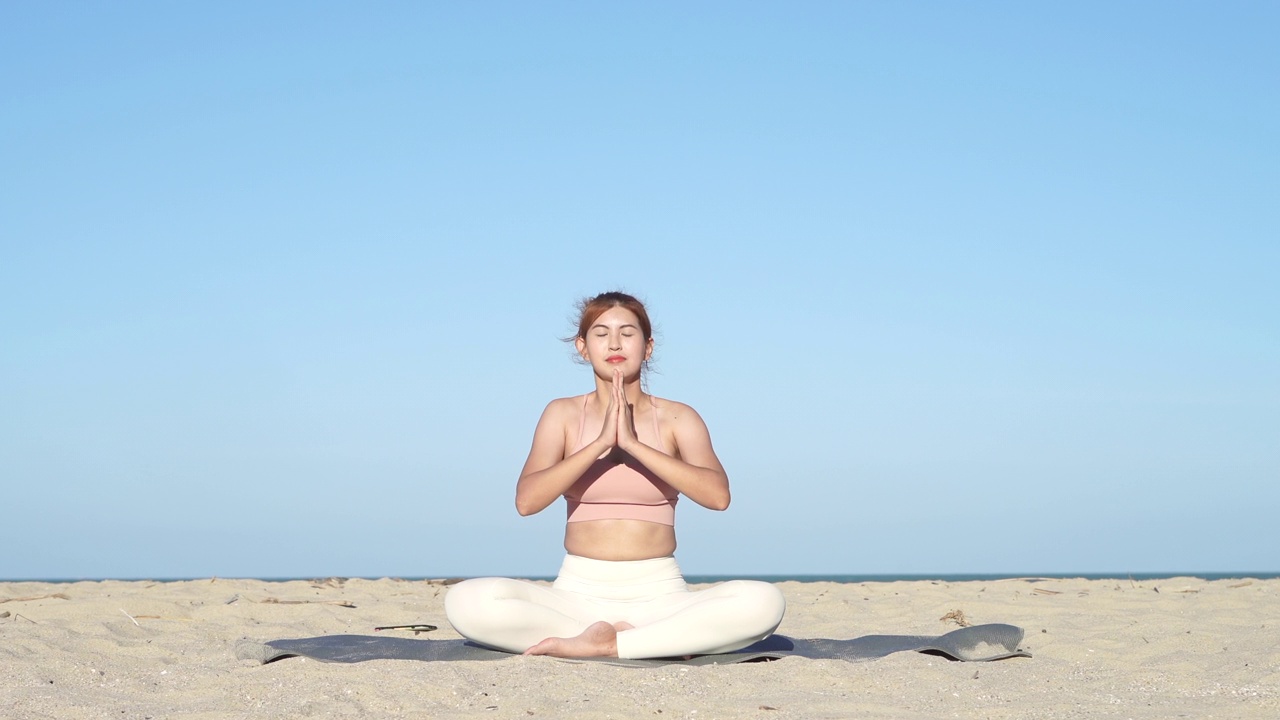 亚洲女人在海边边聊天和做瑜伽，背景是海浪的海洋，在日落时在海边冥想，使她的心平静和和平。视频素材