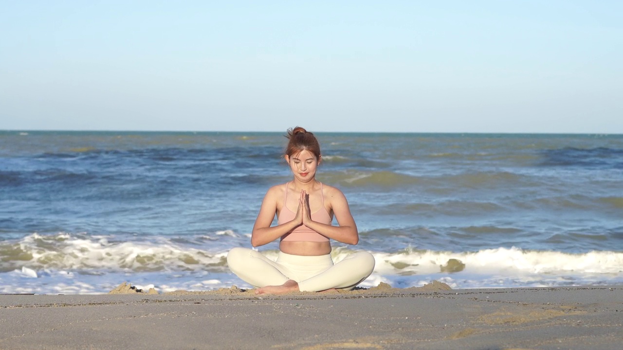 亚洲女人在海边边聊天和做瑜伽，背景是海浪的海洋，在日落时在海边冥想，使她的心平静和和平。视频下载