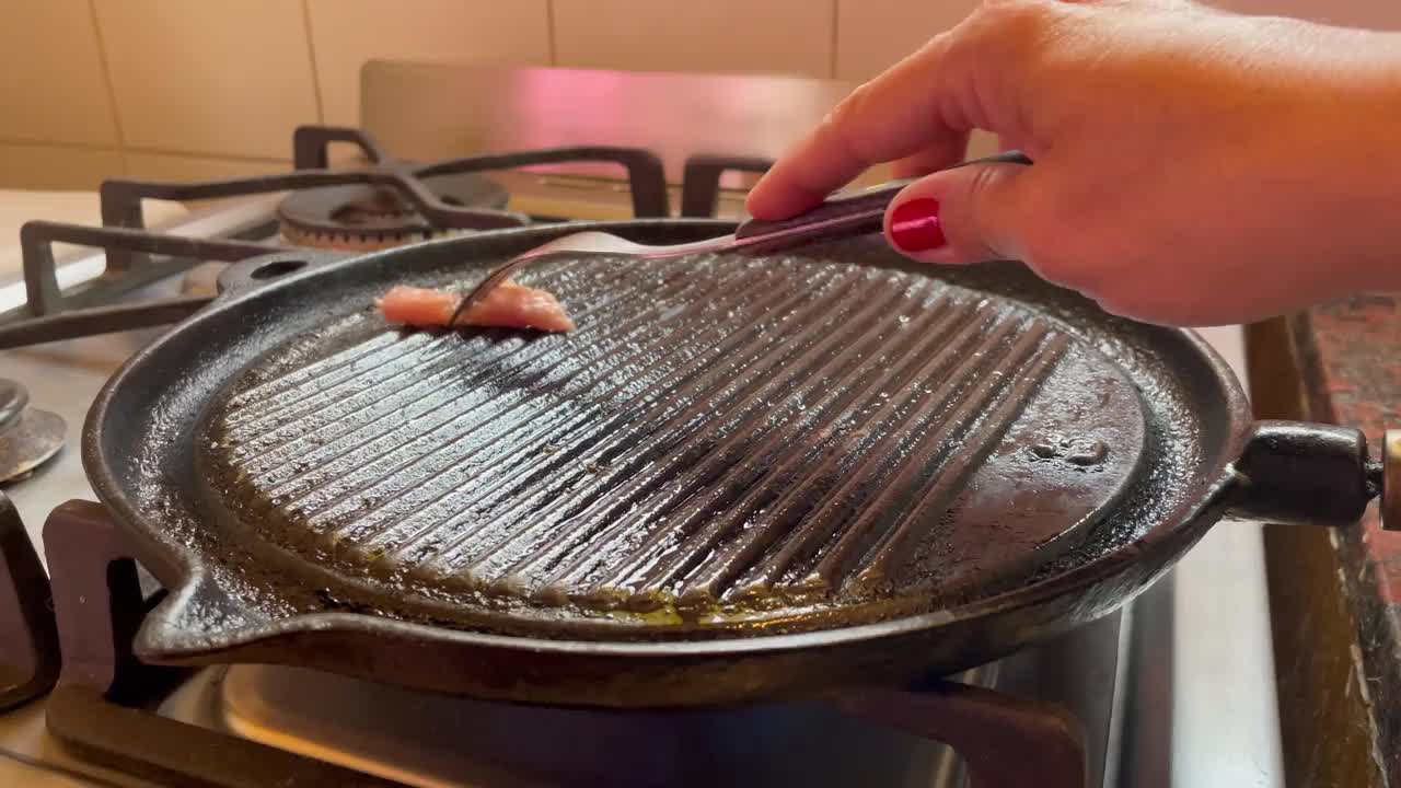 女人用一块脂肪在铸铁锅上涂油，防止肉粘在铸铁上。近距离拍摄，4K分辨率。视频素材