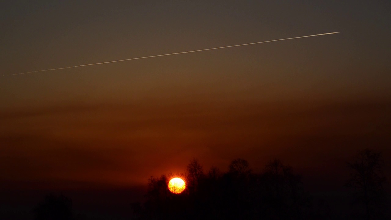 当飞机在高空飞行时，太阳在森林里淡红色的日落视频素材