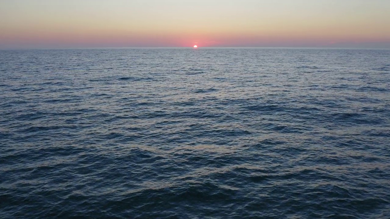 夕阳西下，天空泛着橘黄色，海浪平静的海面上的空中飞行。视频素材