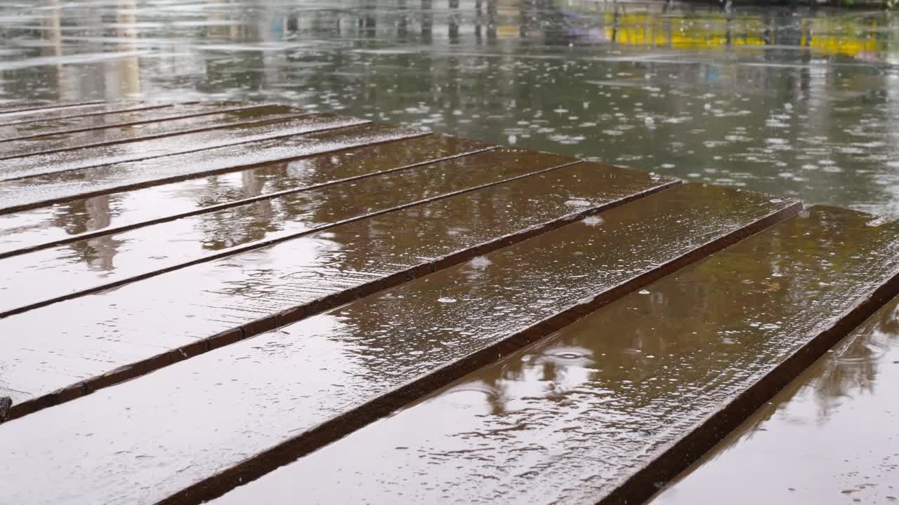 细雨落在露台的木地板上的特写镜头。城市里下着大雨，雨滴落在柏油路和棕色的木地板上视频素材