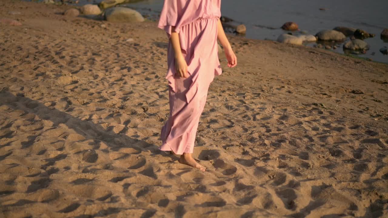 浪漫的女孩享受海风，穿着粉红色的长裙漫步在沙滩上视频素材