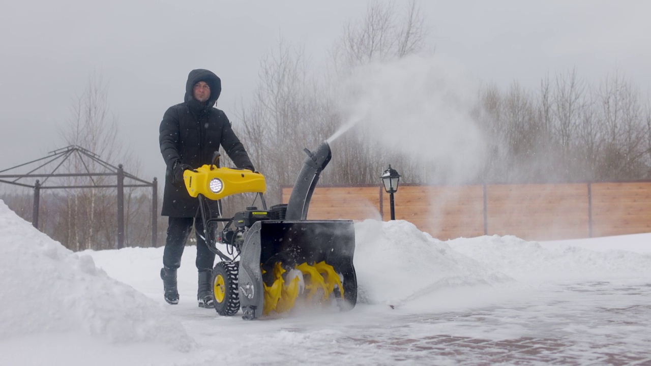 在下雪的时候，一名男子在院子里用吹雪机清理积雪。前视图。慢动作视频素材