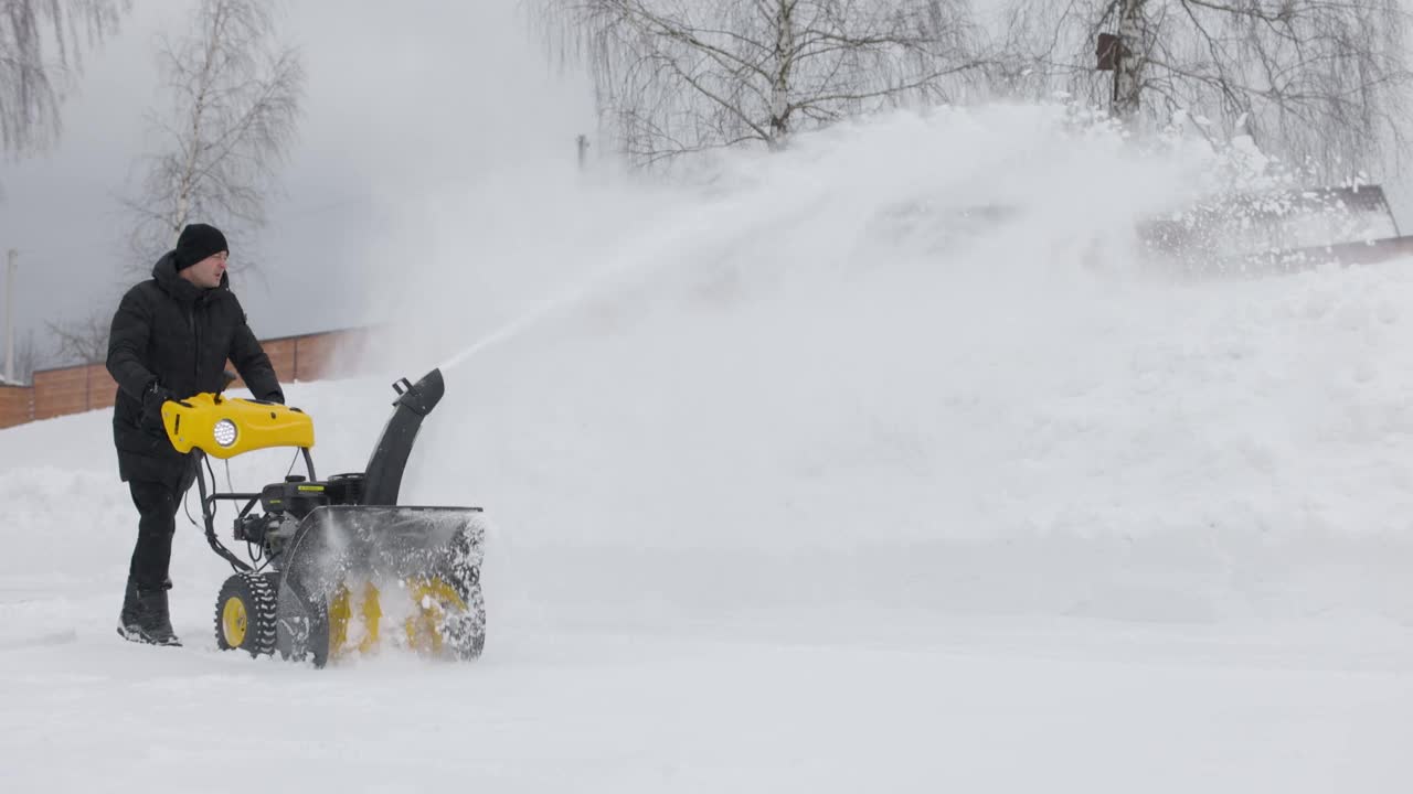 在下雪的时候，一名男子在院子里用吹雪机清理积雪。前视图。慢动作视频素材